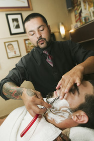 Hispanic barber shaving mans face